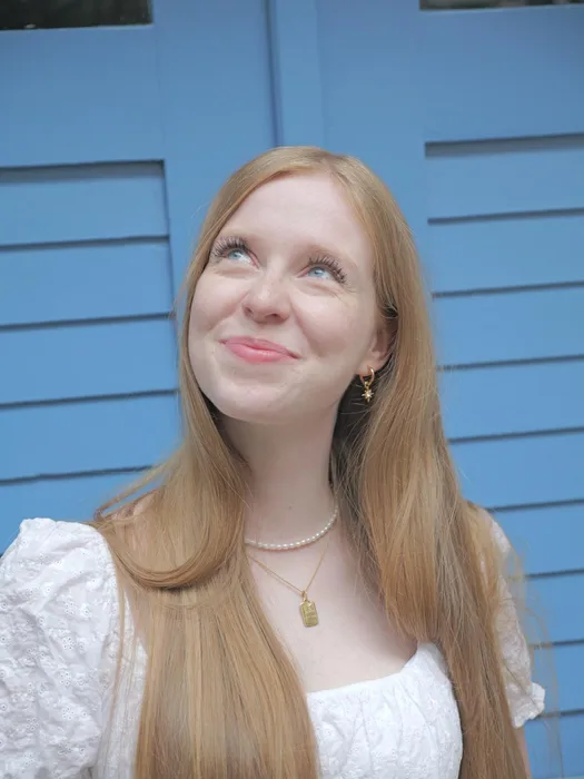 Josefin Schäferhoff in weißer Bluse vor blauen Fensterläden, lächelt nach oben